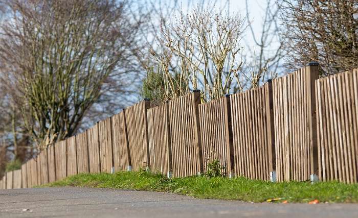 Landscape shot of a brown wooden fence of a mini forest with a clear blue sky